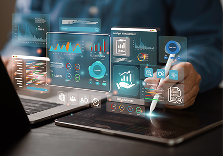 A person uses a stylus on a tablet displaying futuristic data analytics graphs and charts, with additional virtual data interfaces floating in the air near a laptop.